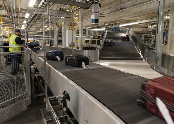 real airport baggage-handling tunnel with moving suitcases, conveyor chutes, a maintenance technician and visible unbranded physical 3D LiDAR sensors in a realistic LiDAR application scene
