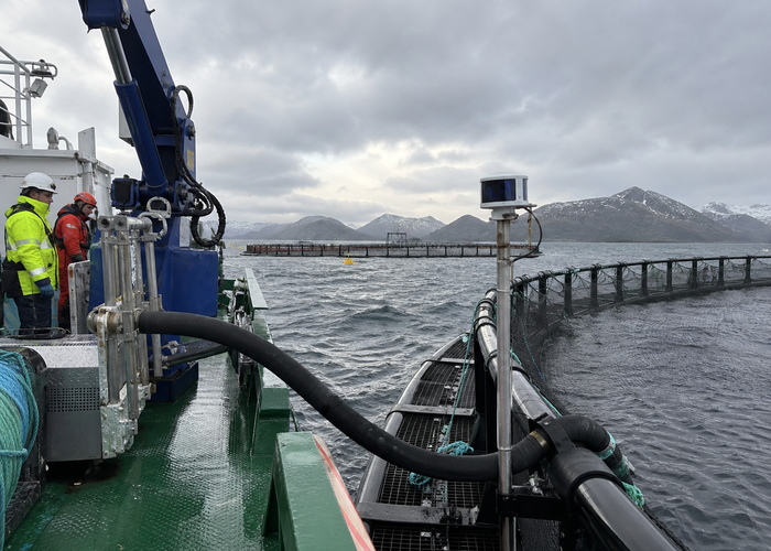 real aquaculture service vessel beside floating fish-farm net pens with unbranded physical 3D LiDAR sensors monitoring deck clearance, feed hoses and walkways validation scene 2