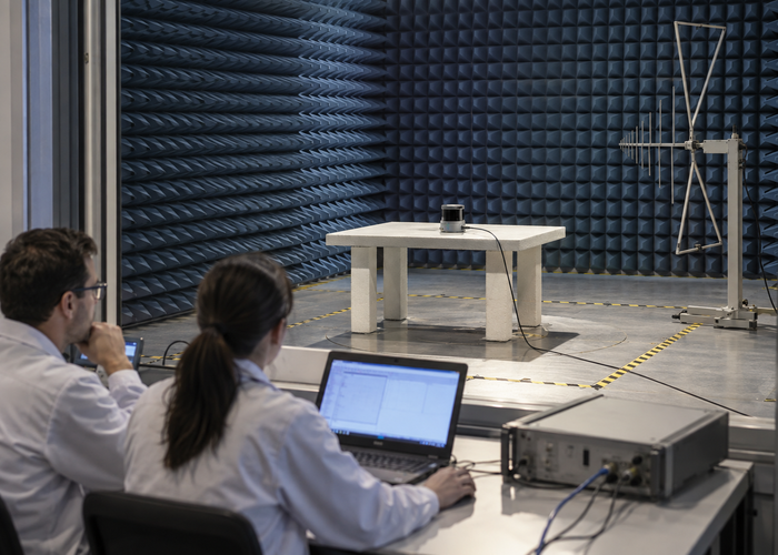 real accredited-style EMC laboratory with an unbranded physical LiDAR sensor under radiated immunity testing and engineers nearby in a realistic LiDAR application scene