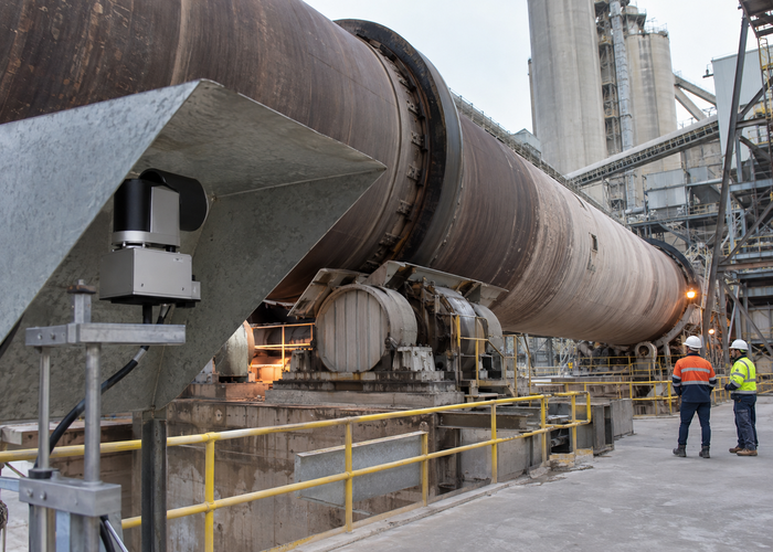 real cement plant rotary kiln area with workers at safe distance and visible unbranded physical industrial LiDAR monitoring equipment in a realistic LiDAR application scene