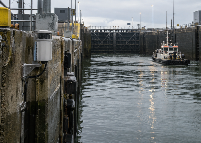 real navigation lock approach with an unbranded physical LiDAR sensor mounted on a concrete guide wall monitoring a workboat aligned between steel gates validation scene 2