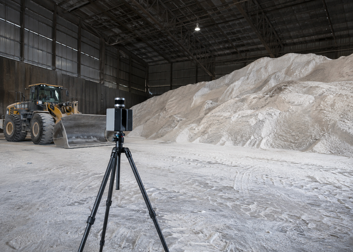 real bulk fertilizer warehouse with floor stockpiles, a loader and a visible unbranded physical LiDAR scanner on a survey tripod validation scene 3