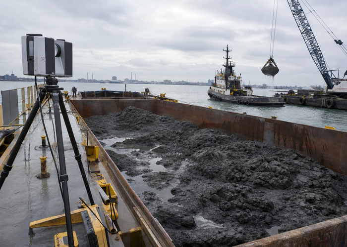real dredging work barge with uneven wet sediment load scanned by a physical unbranded LiDAR from a safe dockside mount in a realistic LiDAR application scene