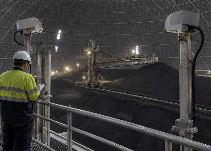 real enclosed petroleum-coke storage dome with dark bulk material, fixed unbranded LiDAR scanners, an inactive reclaim zone and technicians observing from a protected control area validation scene 3