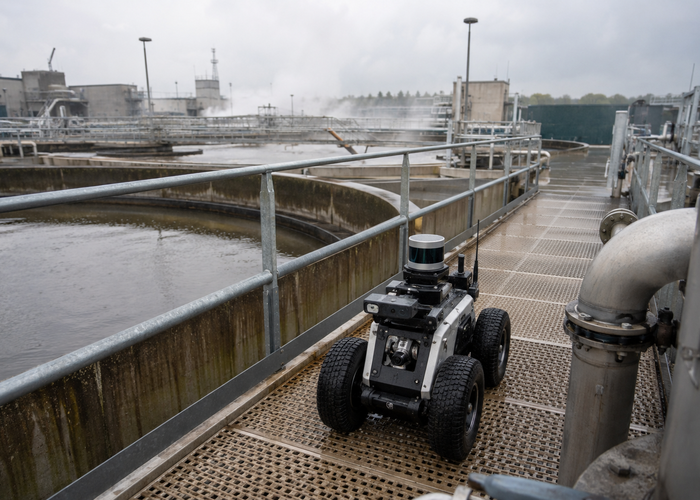 rugged inspection robot using physical LiDAR on a wet wastewater-treatment walkway beside tanks and safety railings in a realistic LiDAR application scene